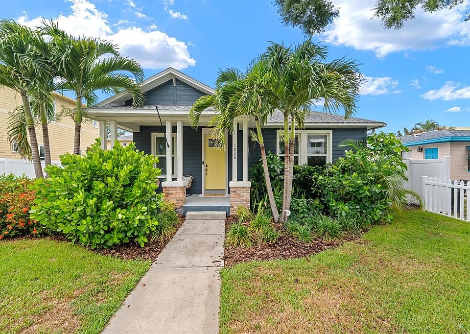 Blue-gray single-story home with yellow front door, covered porch and palms